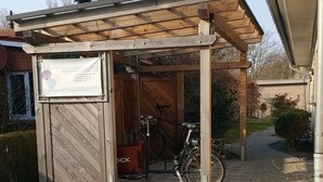 Een houten constructie met een naambord, een fiets en een rode gereedschapskist.