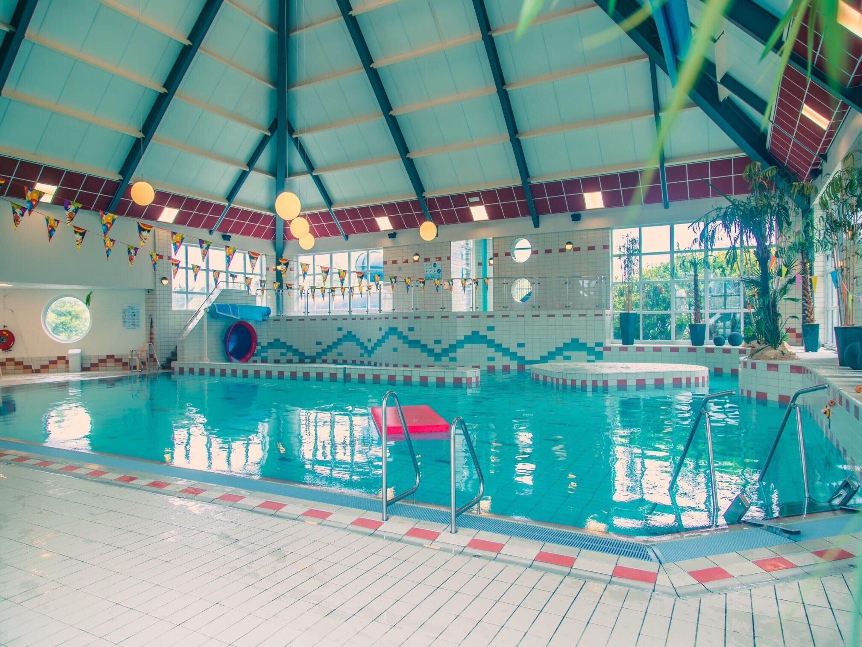Una piscina interior con techos altos, paredes de azulejos y un tobogán.