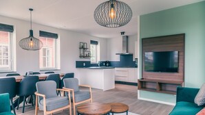 Ein modernes Wohnzimmer mit einer Couch, Sesseln, einem Couchtisch und einem an der Wand befestigten Fernseher.