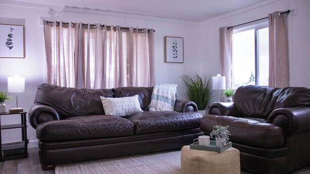 A living room with a brown leather sofa, a small ottoman, and a side table with a lamp. - Cozy 2-bedroom mobile home in lovely Encampment with AC, WiFi (Encampment)