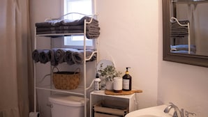 A bathroom with a white shelf holding towels, a basket, and toiletries. - Cozy 2-bedroom mobile home in lovely Encampment with AC, WiFi (Encampment)