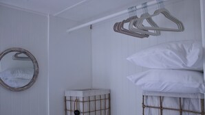 Una habitació amb una estant per a la roba penjada, un mirall rodó, un moble d'emmagatzematge i un llit amb roba de llit blanca.