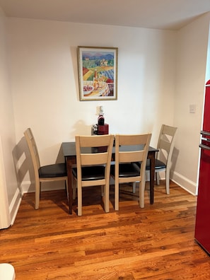 Uma sala de jantar com uma mesa e cadeiras de madeira, um quadro na parede e um eletrodoméstico vermelho.