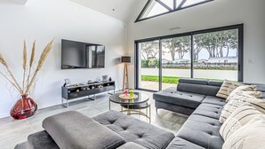 A modern living room with a sectional sofa, a flat-screen TV, and a large window offering a view of the outdoors. - Les Voiles by Interhome (Quiberon)