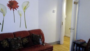 A living room with a red leather sofa, a small table with a book, and a door leading to another room. - House - Sleeps 5, Private Garden & Free Parking (London)