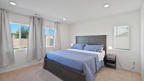 Une chambre à coucher avec un lit, une table de chevet, une fenêtre avec des stores et une vue sur l’extérieur.