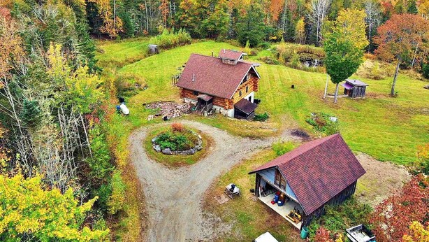 Il s’agit d’une propriété rurale comprenant deux bâtiments principaux : une grande maison en bois et un petit abri, le tout entouré d’une pelouse bien entretenue et d’une variété d’arbres aux couleurs automnales.