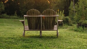 Une chaise Adirondack en bois, placée dans un champ herbeux, avec des arbres en arrière-plan.