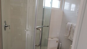 Une salle de bain moderne avec une douche à parois de verre, des toilettes et une petite fenêtre.