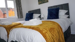 A hotel room with two beds, a window with curtains, a painting on the wall, and a view of trees outside.