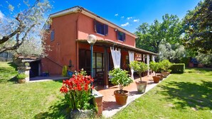 Una casa de dos pisos con fachada roja, un porche cubierto y un jardín con macetas y flores.