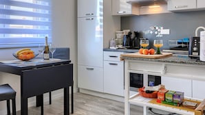Une cuisine moderne avec des meubles blancs, une table à manger avec des chaises, un panier de fruits et une machine à café.