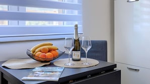 Une table à manger avec une bouteille de vin, deux verres, un saladier de fruits et un magazine.