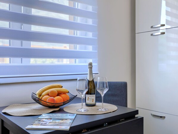 A dining table with a bottle of wine, two glasses, a bowl of fruit, and a magazine.