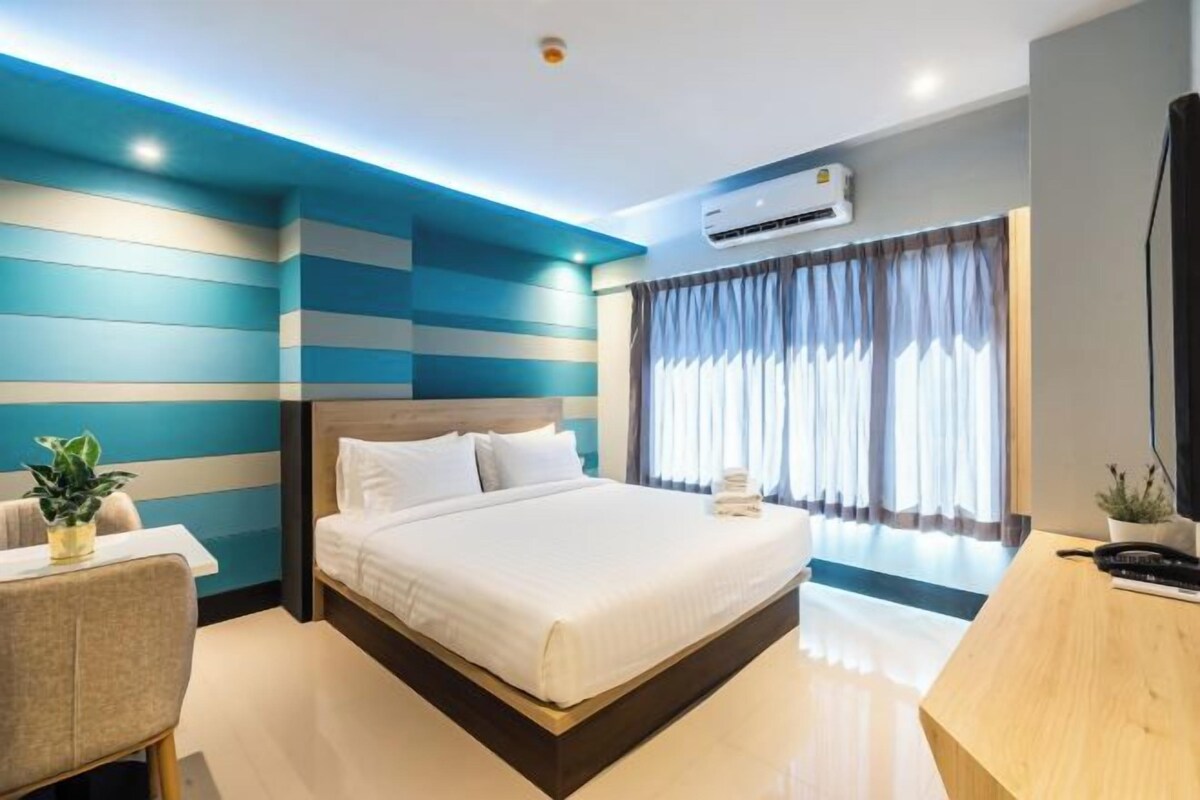 A modern hotel room with a large bed, a desk, and a potted plant.