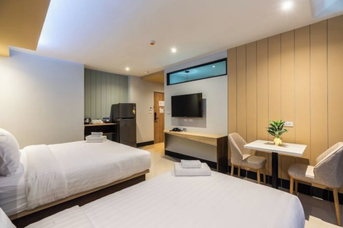 Habitación de hotel con dos camas, un escritorio, un televisor y una pequeña mesa con una planta.