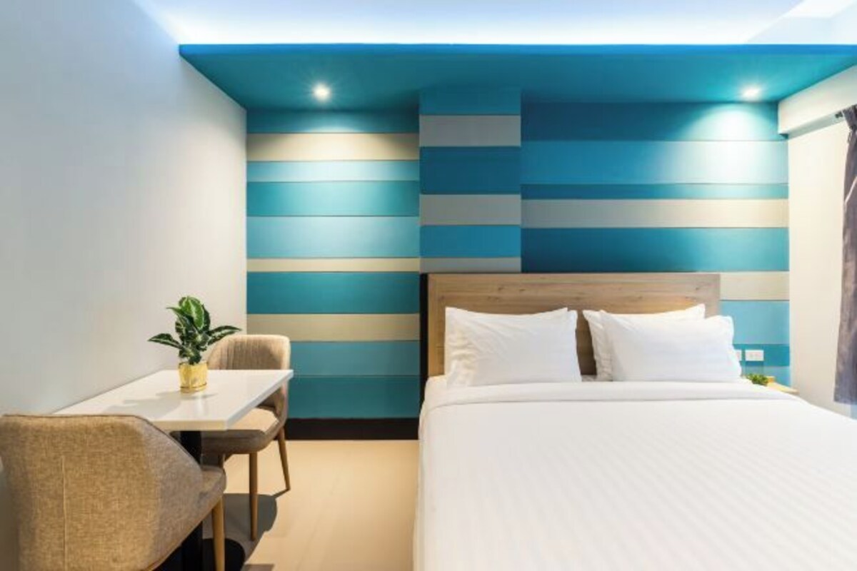 Una habitación de hotel con una cama, una mesita con una silla y una planta.