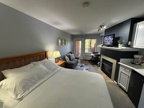 Quarto de hotel com cama, escrivaninha, sofá, televisão e cozinha.