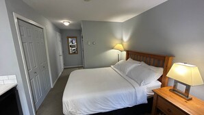 A bedroom with a bed, bedside lamps, a wooden nightstand, and a door. - Quiet Studio on Golf Course - 212B (Kelowna)