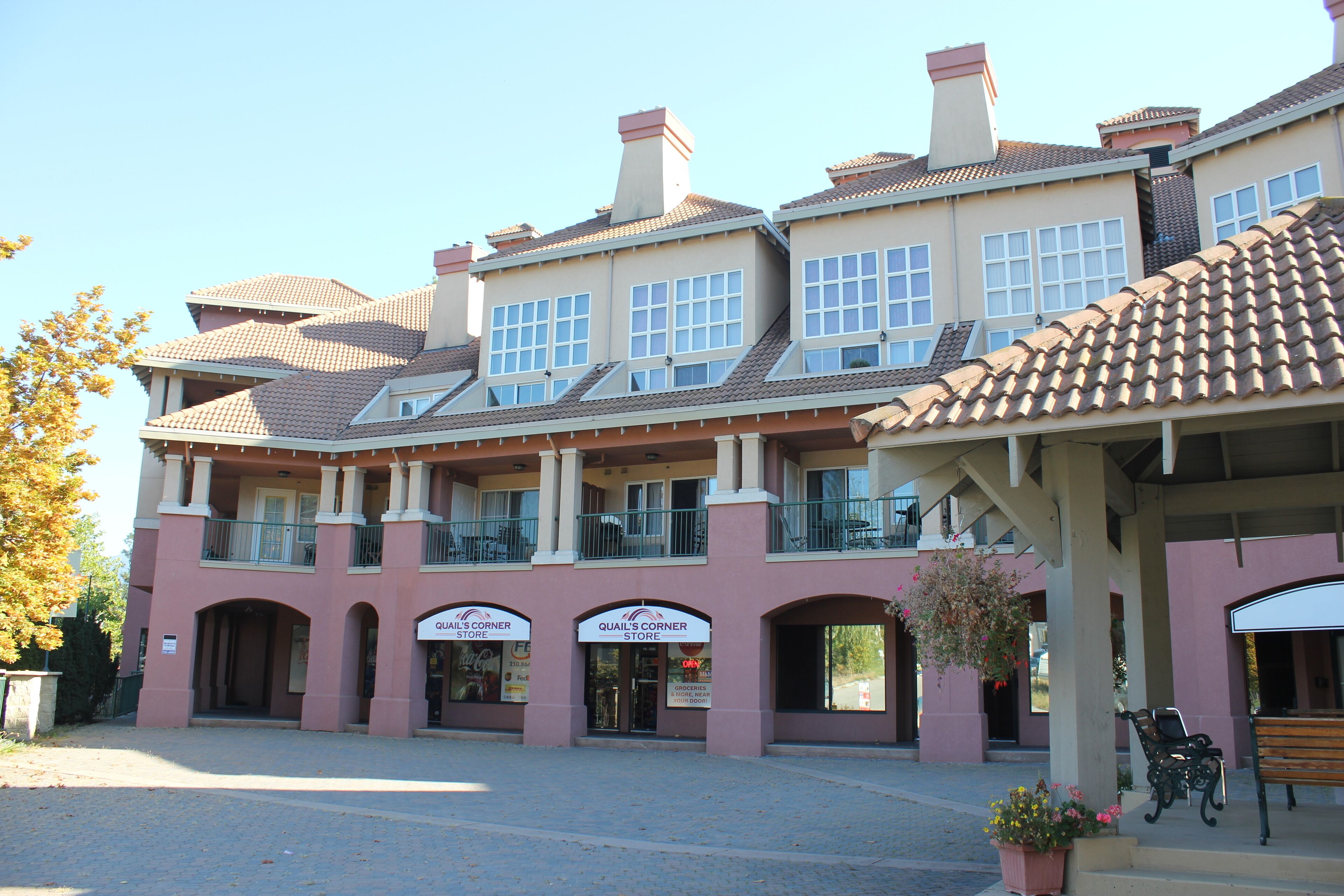A building with multiple storefronts, including Quail's Corner Store, with a covered entrance and outdoor seating area.