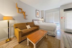 A bedroom with a bed, a sofa, a coffee table, a floor lamp, and a window with blinds.