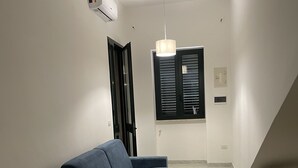 Un salon moderne avec un canapé bleu, un meuble en bois et une fenêtre équipée de stores.