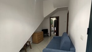 Un vaste espace de vie agrémenté d’un canapé bleu, d’une commode en bois et d’un luminaire suspendu.