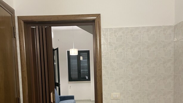 Une pièce avec une table en bois, un canapé bleu et une vue sur une autre pièce dotée d’une fenêtre et d’un luminaire suspendu.