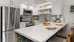 A modern kitchen with stainless steel appliances, white cabinetry, and a herringbone-patterned backsplash. - SUMMER SALE! Remodeled Condo w Ocean Views Pool AC - Papakea  J106 (Lahaina)