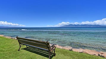 A bench by a clear blue sea with a distant mountain range.