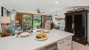 A modern kitchen with a marble countertop, dining area, and a view of a garden. - SUMMER SALE! Remodeled Condo w Ocean Views Pool AC - Papakea  J106 (Lahaina)