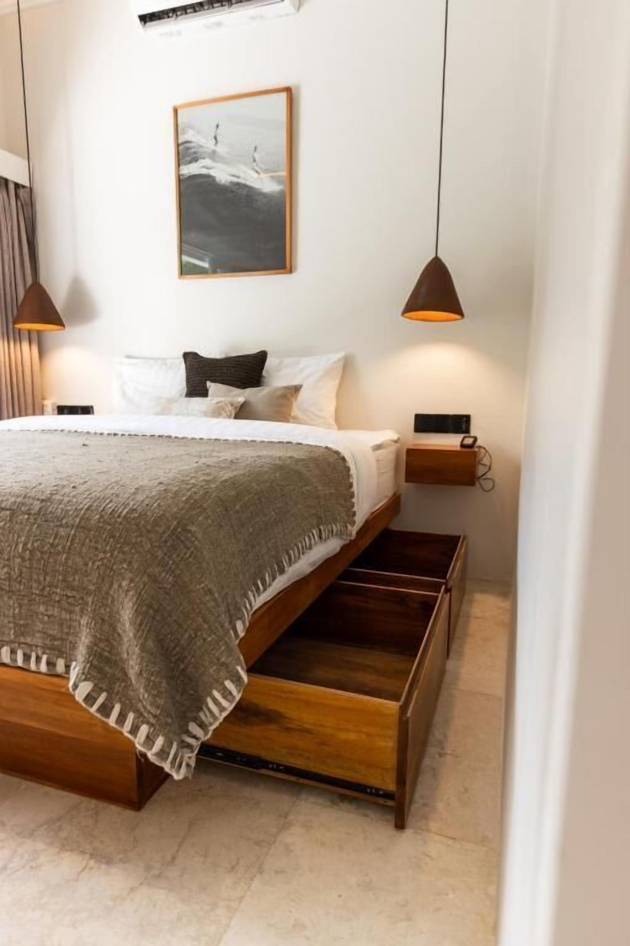 Un dormitorio con cama, mesitas de noche, una lámpara colgante y un cuadro en la pared.