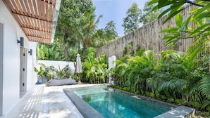 Una piscina rettangolare con bordatura in pietra, circondata da vegetazione rigogliosa e una recinzione in legno.