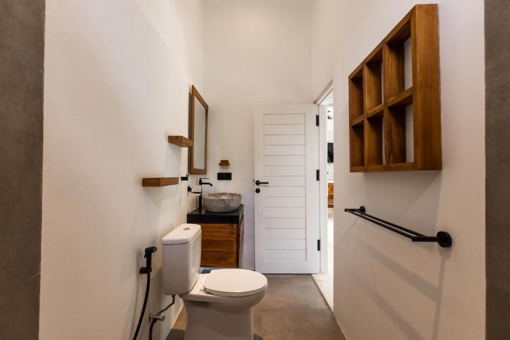 A narrow bathroom with a toilet, sink, and wooden shelves.