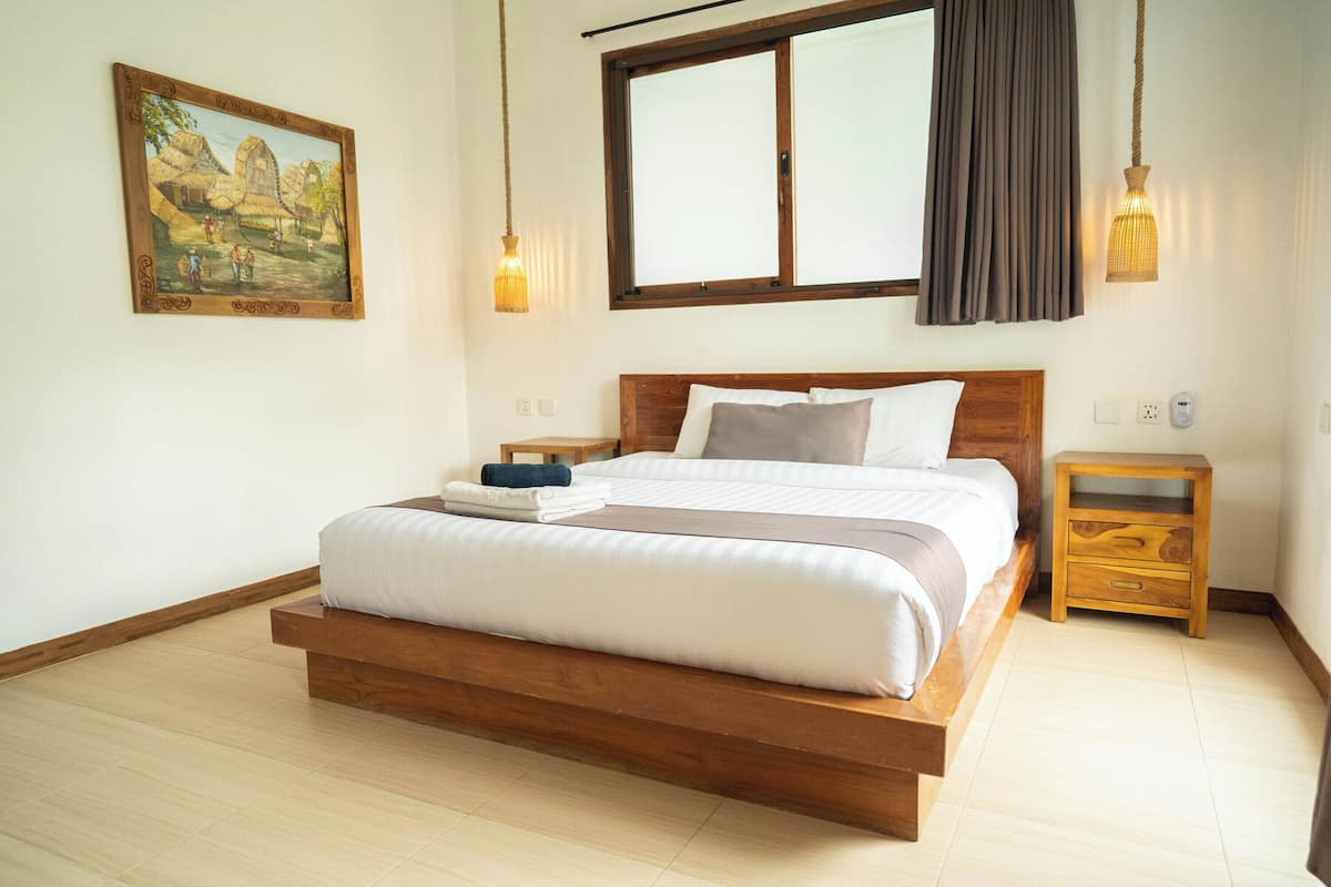 A bedroom with a wooden bed, a nightstand, a painting, and a window with curtains.