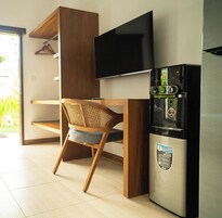 Una kitchenette compacta con un refrigerador moderno, un televisor de pantalla plana y una silla de madera con respaldo tejido.
