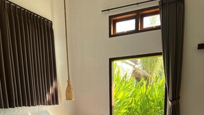 Un letto rifatto con cura, asciugamani a forma di cigno e di fiore di loto, un comodino con una lampada, e vista su un giardino rigoglioso attraverso una porta scorrevole.