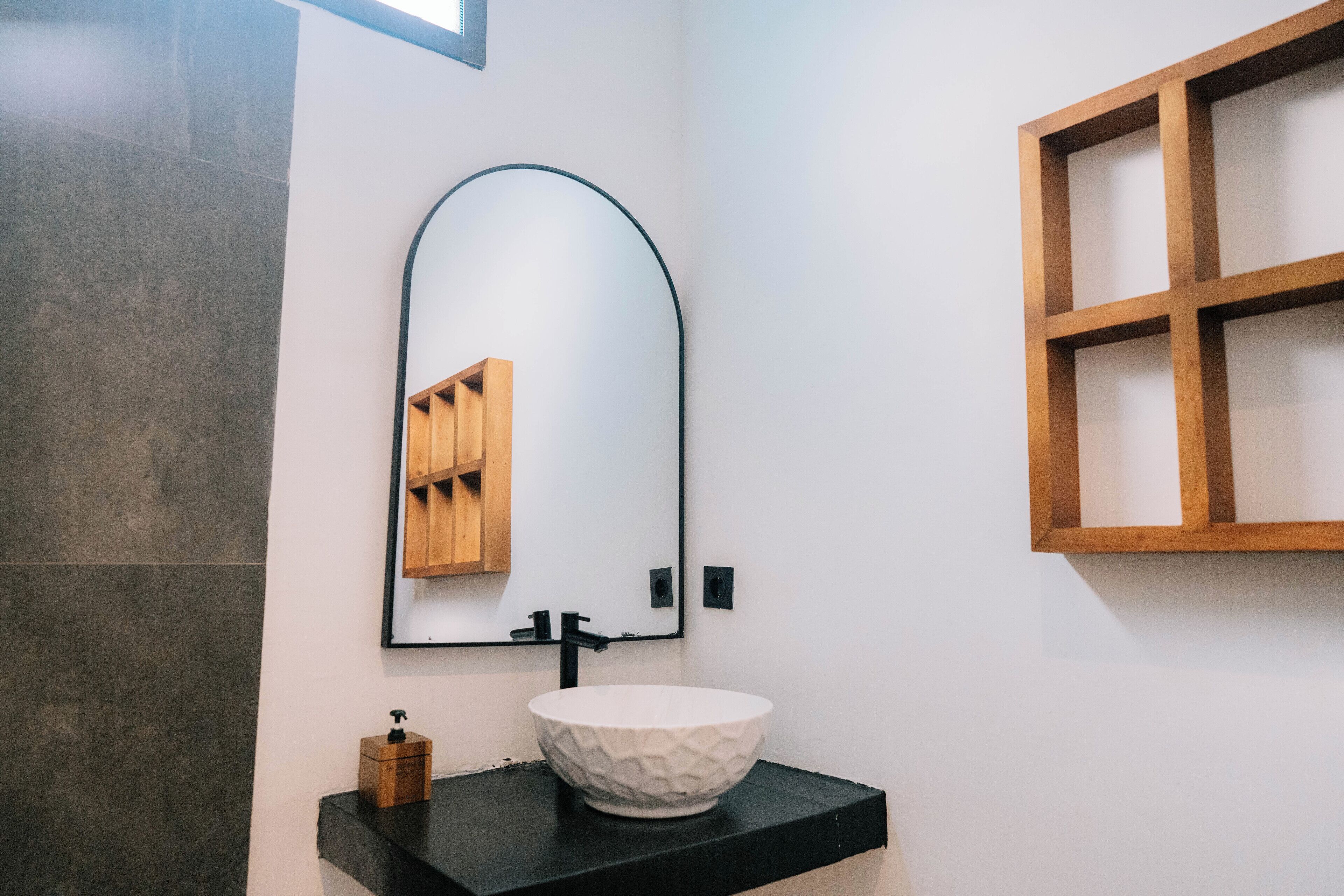 A bathroom with a white sink, black countertop, and a mirror with a wooden frame.