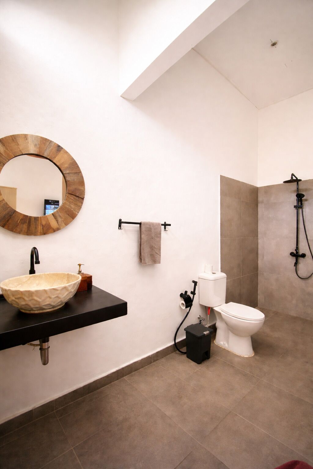 Een moderne badkamer met een ronde spiegel, een zwart aanrecht, een beige wastafel, een toilet en een douche.