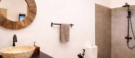 Une salle de bain moderne avec un miroir rond, un plan de toilette noir, un lavabo beige, des toilettes et une douche.