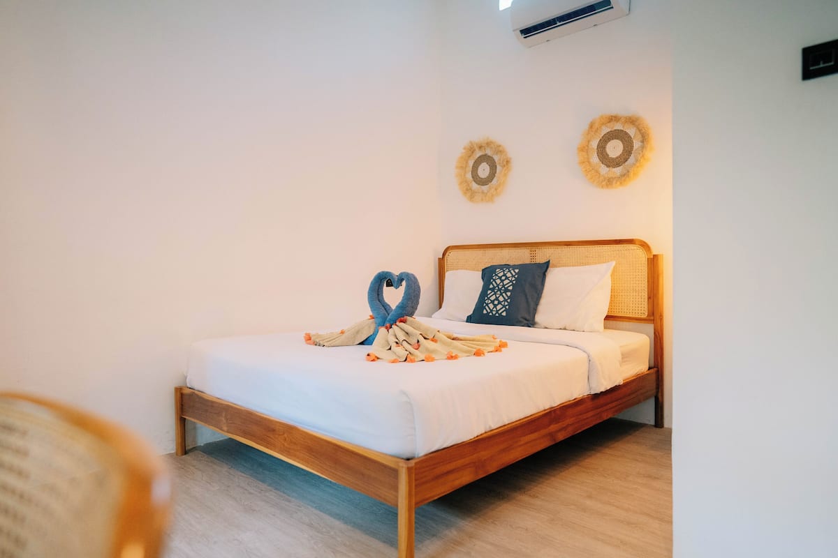 A neatly made bed with a heart-shaped towel and a swan towel design, two decorative wall hangings, and a wooden headboard.