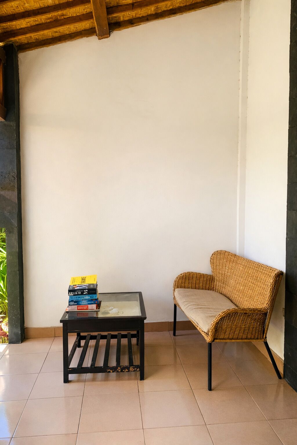 Una stanza con un divano in vimini, un tavolo con piano in vetro e libri, e un pavimento piastrellato.