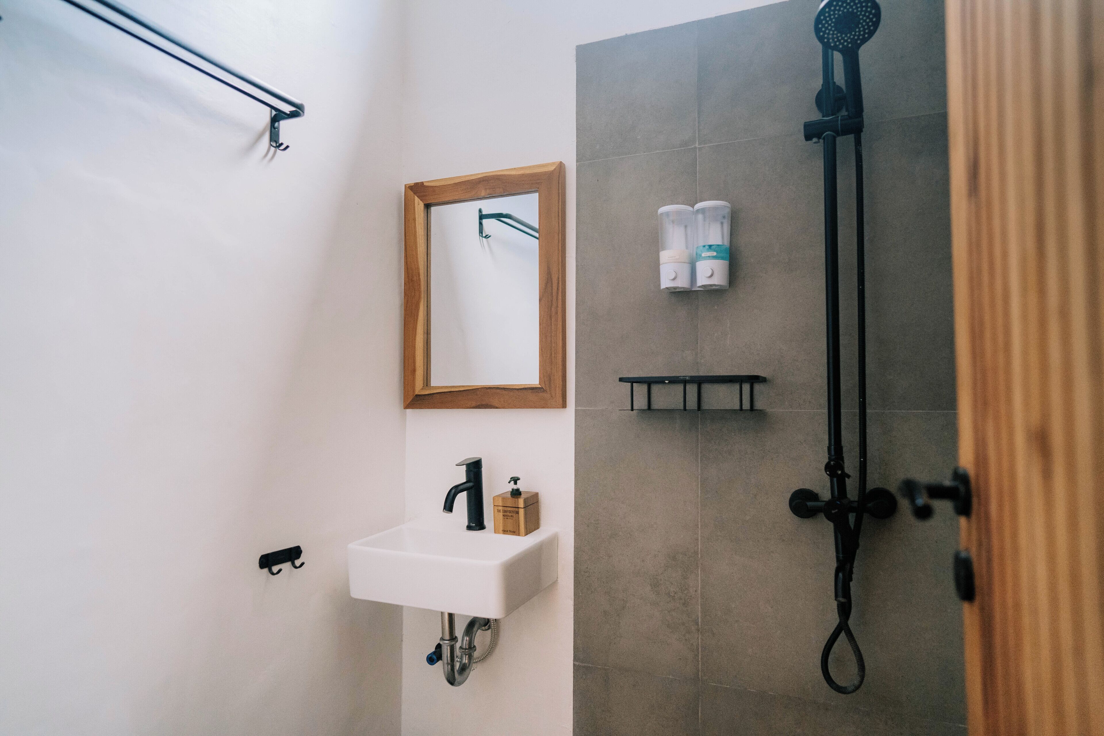 A modern bathroom with a white sink, a wooden-framed mirror, a shower with a handheld showerhead, and a towel rack.