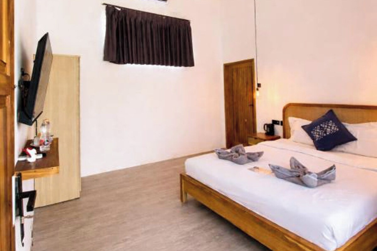 A bedroom with a bed, a ceiling fan, an air conditioning unit, a TV, and a wooden wardrobe.