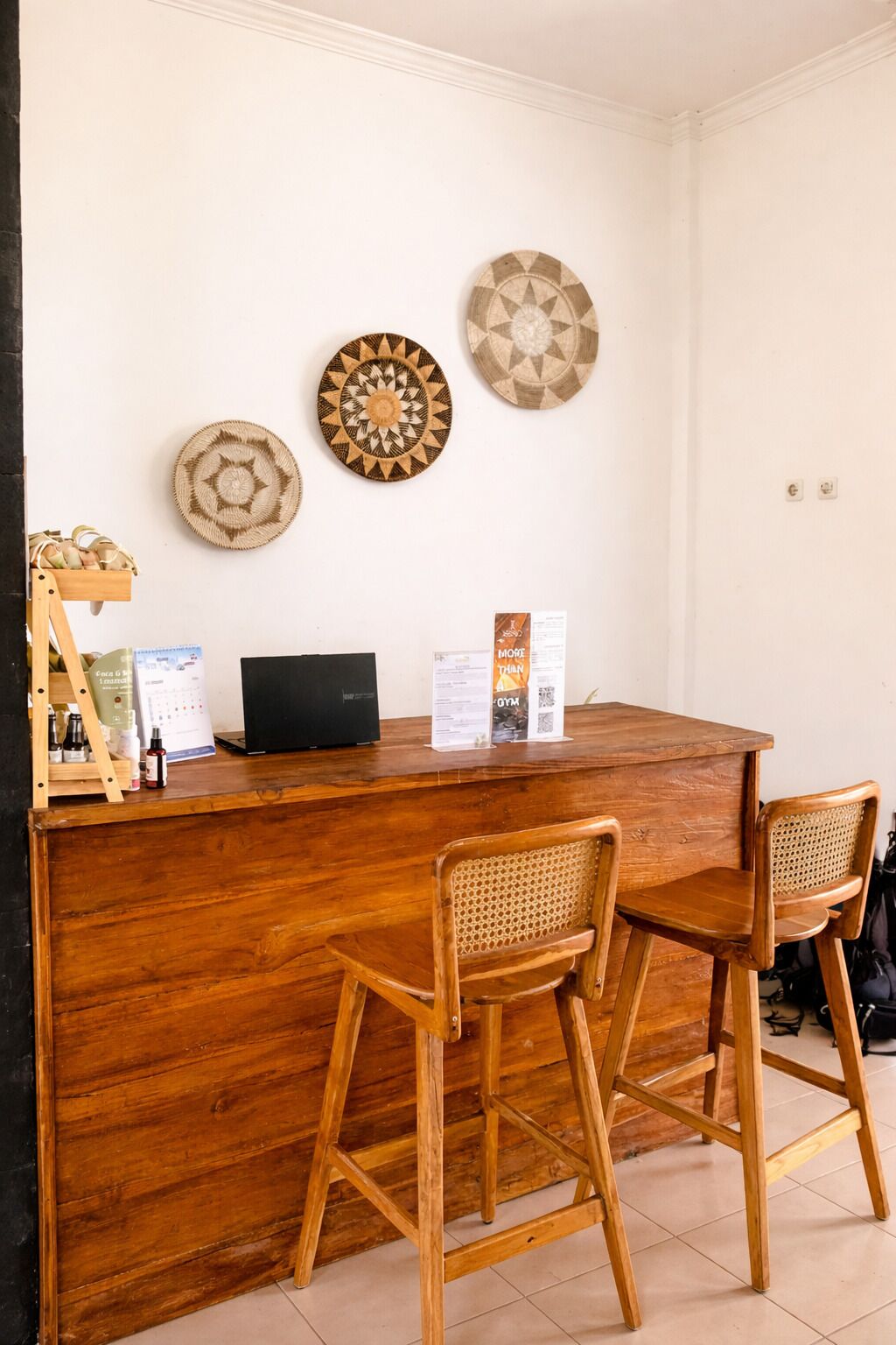 A wooden reception desk with two wicker chairs, a laptop, and wall decorations.