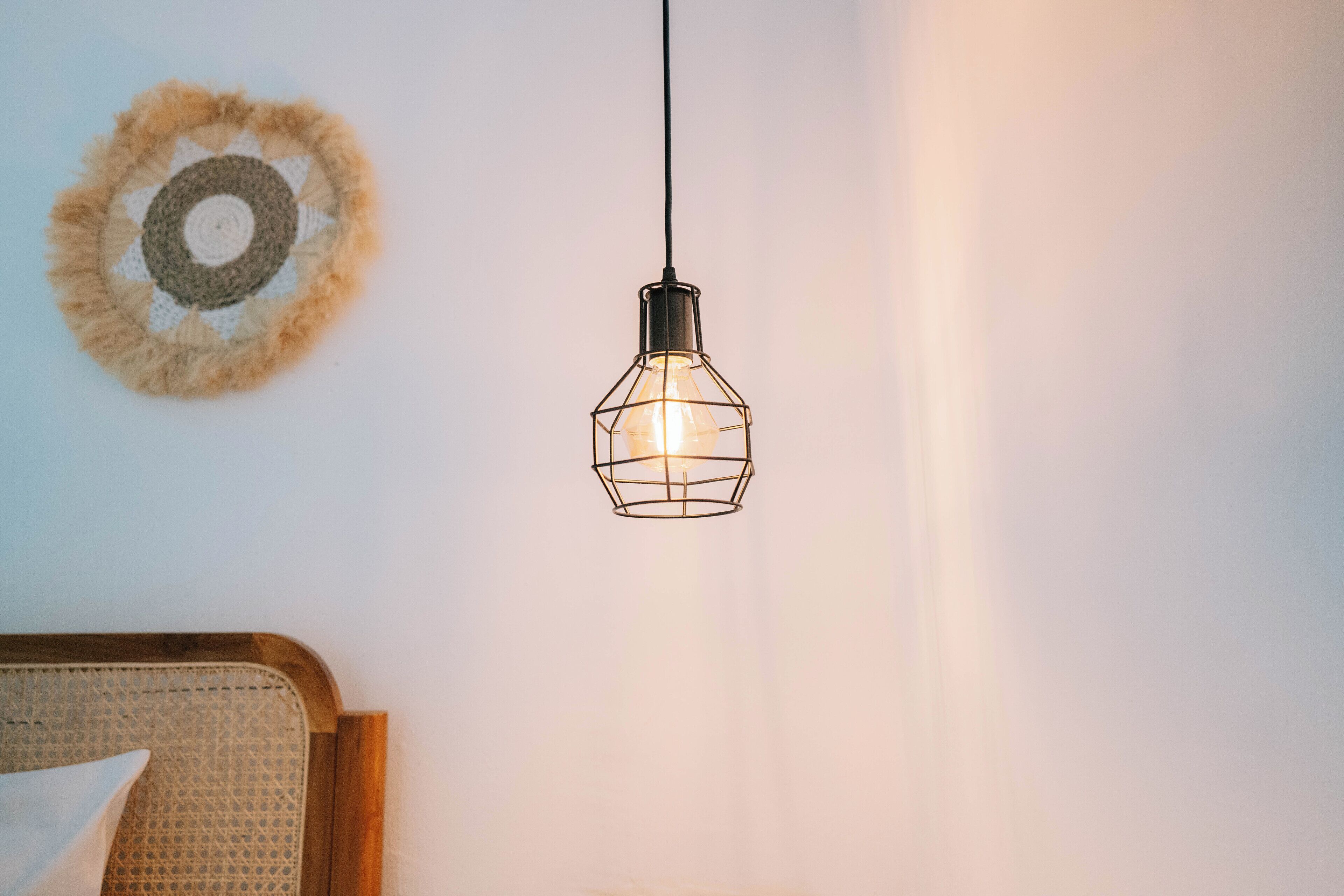 A hanging light fixture with a geometric design, a woven wall decoration, and a wooden headboard.