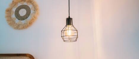 A hanging light fixture with a geometric design, a woven wall decoration, and a wooden headboard.