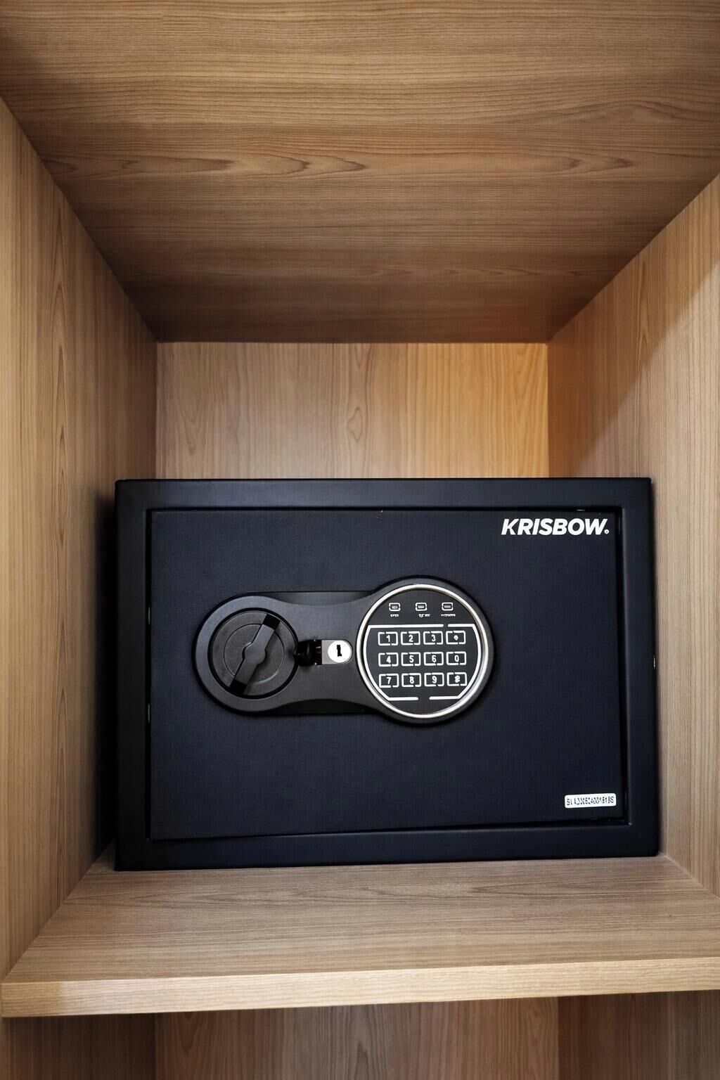 Una caja fuerte negra con un dial de combinación y un teclado, con la etiqueta "KRISBOW", dentro de un mueble de madera.