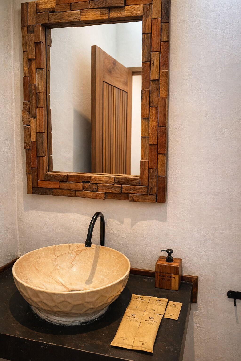 Un baño con un lavabo grande y redondo de mármol color crema, un espejo con marco de madera y un dispensador de jabón de madera.