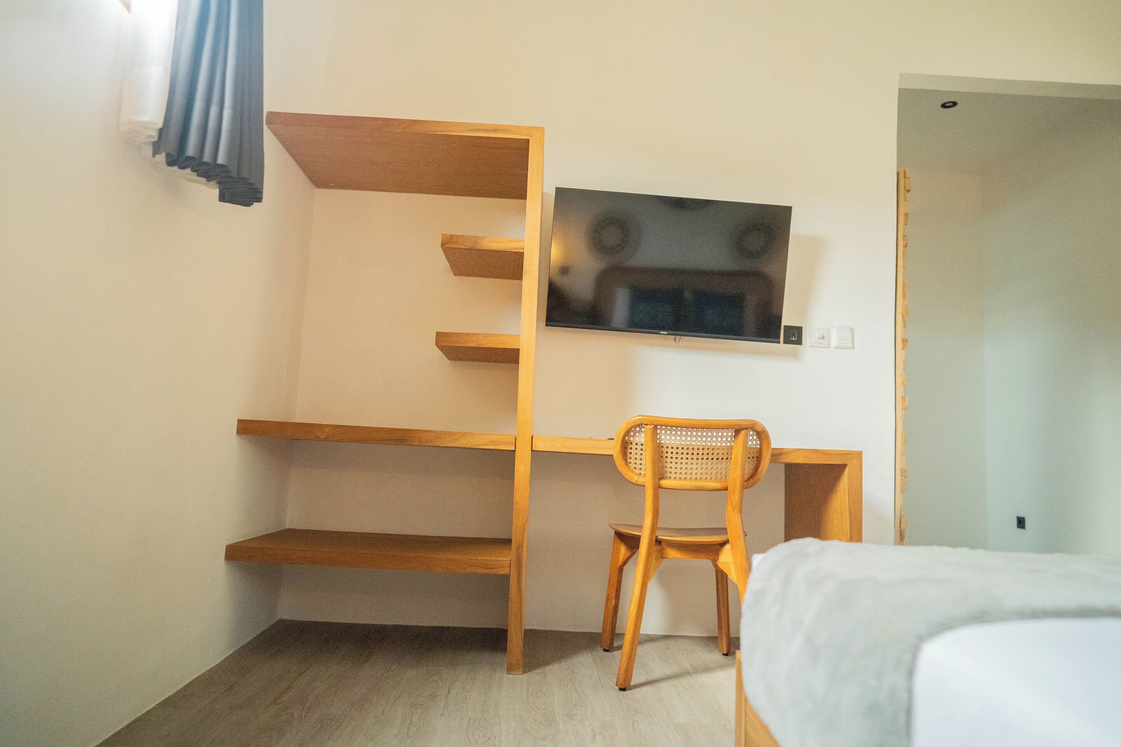Un dormitorio con una cama, un escritorio de madera con estantes, una silla y un televisor montado en la pared.